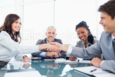 Two young executives shaking hands in front of their director an