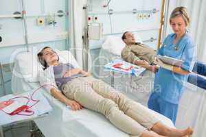 Nurse next to a transfused patient writing on a clipboard