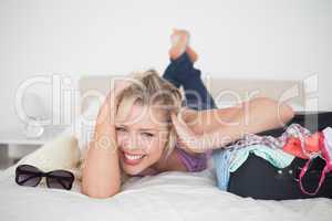 Laughing young woman lying next to her full suitcase