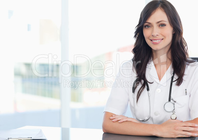 Young smiling doctor sitting at the desk near a clipboard
