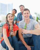 A laughing group sitting on the couch and the floor with beers i