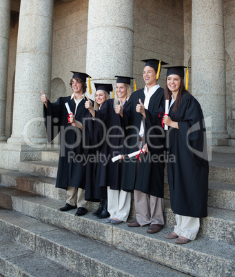 Laughing graduates posing the thumb-up