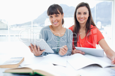 A pair of smiling girls doing work with tablets as they look int