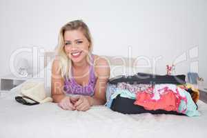 Blonde lying on her bed next to a full suitcase