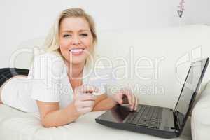 Casual woman lying with a credit card and a laptop