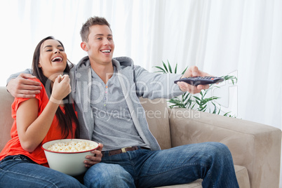 A laughing couple enjoying a tv show together as they hold each