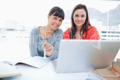 Two girls sitting in front of the laptop while they look into th