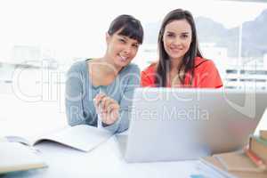 Two girls sitting in front of the laptop while they look into th
