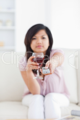 Blurred woman holding a glass of red wine and a television remot