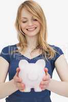 Blonde woman holding a piggy bank while looking it