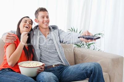 An embracing laughing couple enjoying a tv show as they eat popc