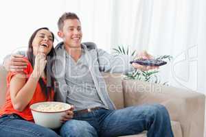 An embracing laughing couple enjoying a tv show as they eat popc