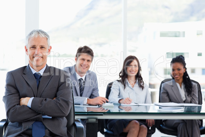 Mature businessman sitting with his arms crossed while his team