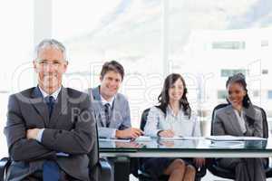 Mature businessman sitting with his arms crossed while his team