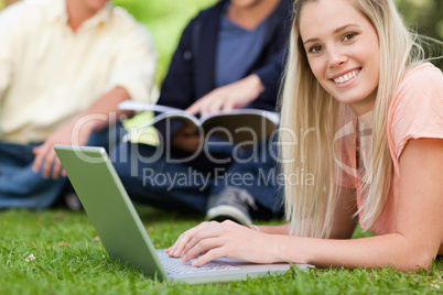 Portrait of a smiling girl using a laptop while lying in a park