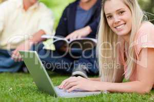 Portrait of a smiling girl using a laptop while lying in a park