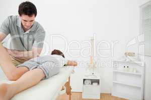 Serious brunette physiotherapist stretching the leg of a patient