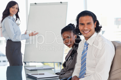 Two smiling employees sitting at a desk in a meeting room during