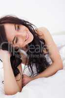 Happy brunette woman lying on her white duvet
