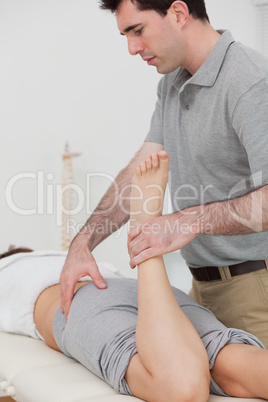 Woman lying while a physiotherapist is bending her leg