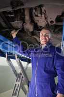 Smiling mechanic repairing with a spanner the below of a car