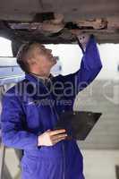 Mechanic looking at the below of a car while holding a clipboard