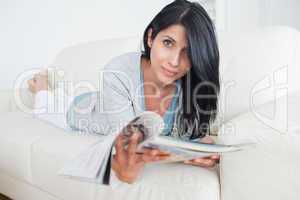 Woman crossing her legs as she lays on a couch and holds a magaz