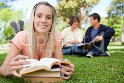 Smiling girl lying in front of her books in a park