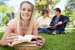 Smiling girl lying in front of her books in a park