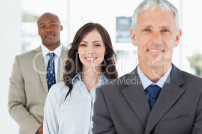 Three smiling business people standing upright and looking ahead