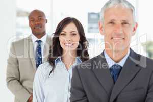 Three smiling business people standing upright and looking ahead