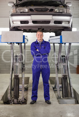 Mechanic standing with arms crossed below a car