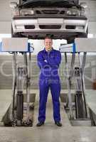 Mechanic standing with arms crossed below a car