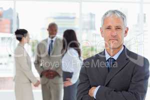 Serious businessman crossing his arms while his team is in the b