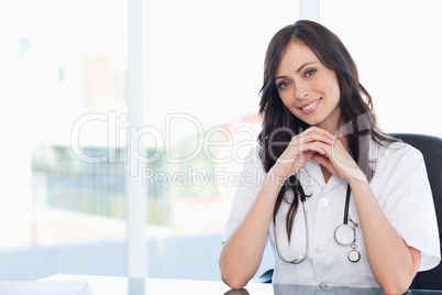 Young nurse sitting at the desk with her hands crossed and leani