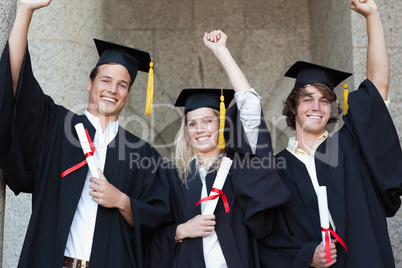 Graduates holding their diploma while raising arm