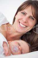 Smiling brunette woman lying while her baby is sleeping