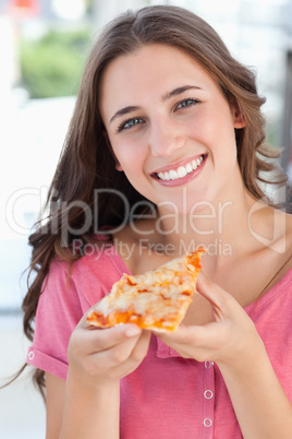 Close up of a woman smiling with a piece of pizza and looking at