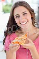 Close up of a woman smiling with a piece of pizza and looking at