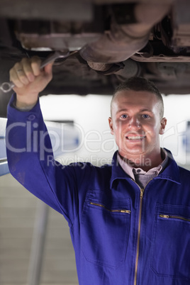 Smiling mechanic repairing the below of a car with a spanner