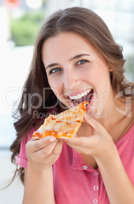 A woman about to eat a piece of pizza as she looks at the camera