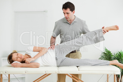 Serious practitioner rising the leg of his patient