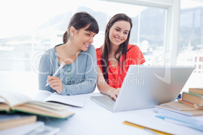 A couple of girls sitting together as they work on the laptop