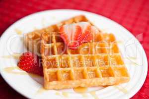 Waffles and half cut strawberry together in a white plate