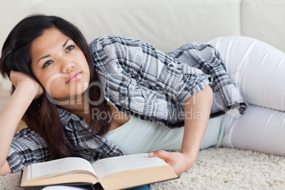 Thinking woman lying on the floor while holding a book