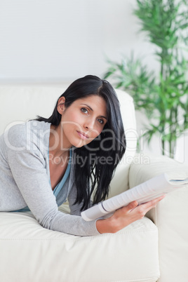 Woman laying on a couch while holding a magazine