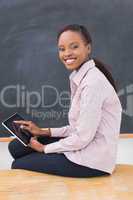 Teacher sitting on desk while holding a tablet computer