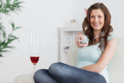Woman pressing a remote control while sitting on a sofa