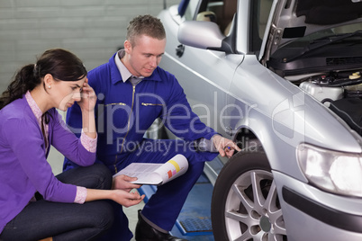 Mechanic looking at the car wheel next to a client