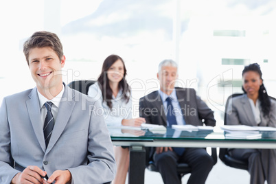 Smiling young businessman sitting in front of his team and looki